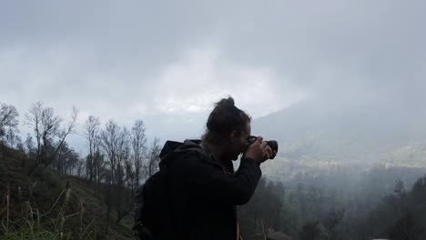 hombre mochilero caucásico tomando una foto en la montaña del bosque de humo brumoso