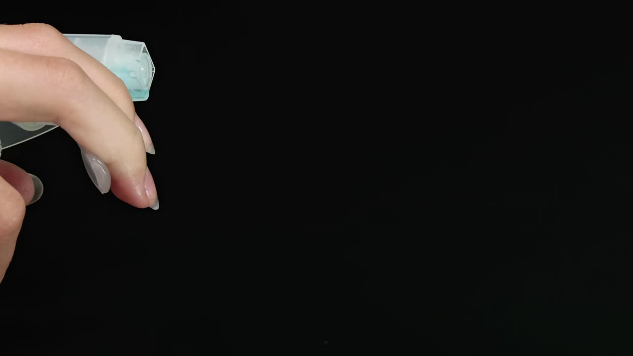A hand operates a spray bottle, releasing a fine mist against a dark background.