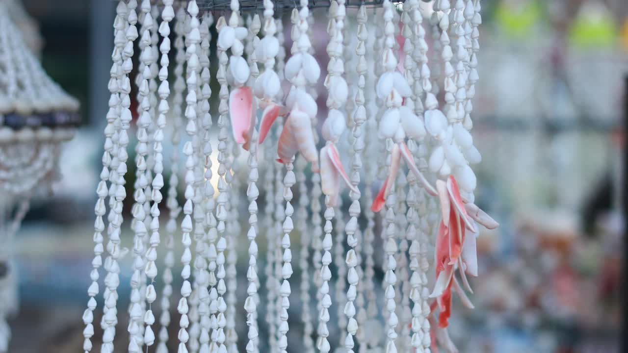 Shell wind chimes gently sway in the breeze, creating a serene atmosphere in a Phuket market setting