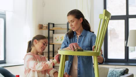 furniture-renovation,-diy-and-home-improvement-concept--happy-smiling-mother-and-daughter-sanding-old-round-wooden-chair-with-sponge-at-home