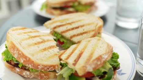 Deliciosos-Sándwiches-Tostados-Con-Verduras-En-Platos-Blancos,-De-Cerca