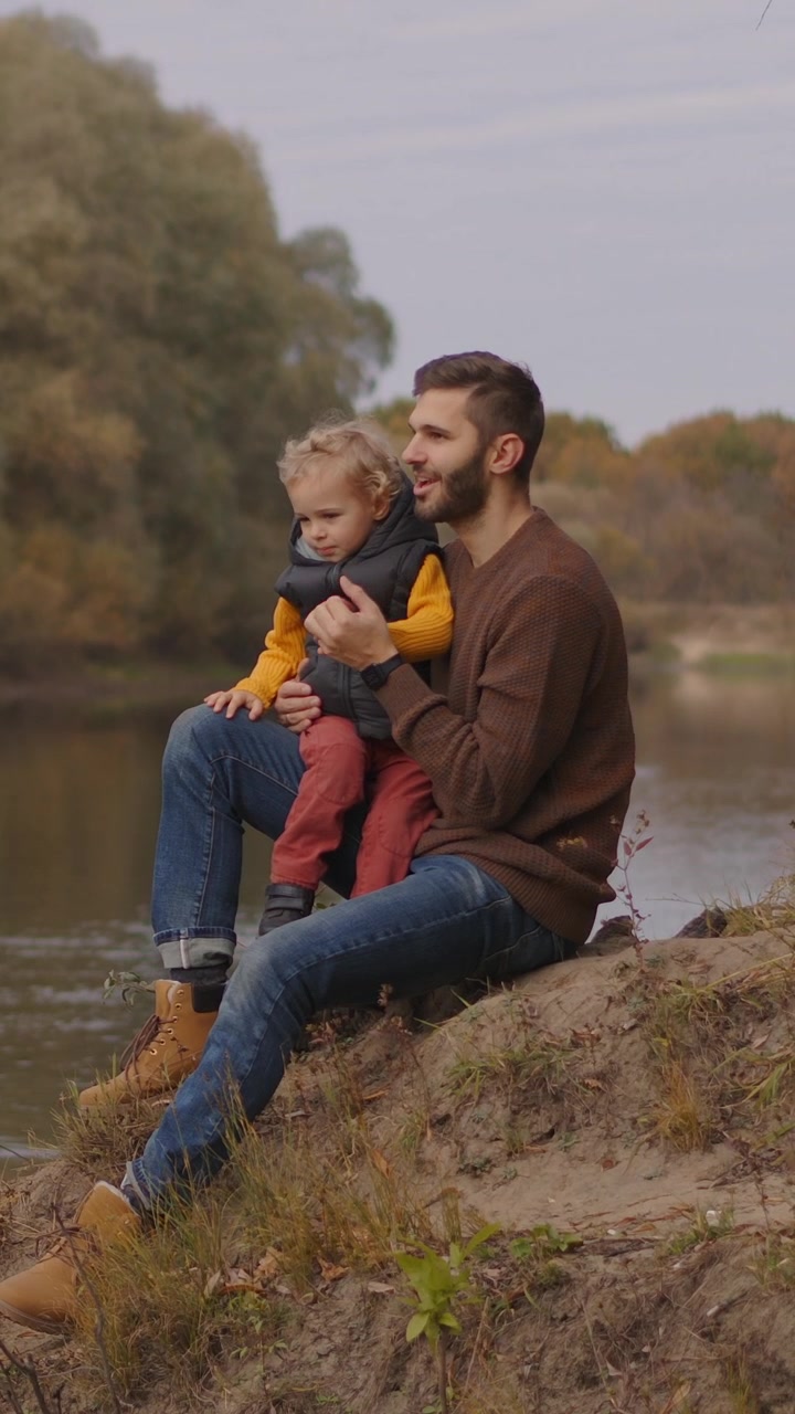 Padre e figlio seduti insieme accanto al fiume in autunno
