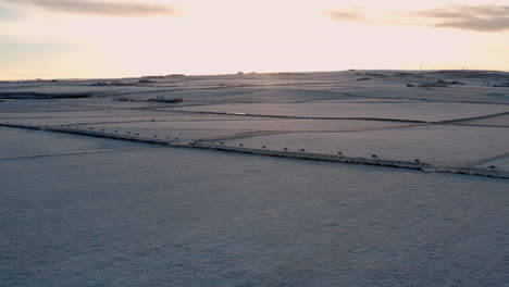 Visión-Aérea-Panorámica-Del-Cielo-Del-Atardecer-Que-Difunde-Una-Luz-Suave-En-Los-Campos-Agrícolas-Cubiertos-De-Nieve