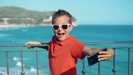 joyful boy taking selfie outdoor. cheerful guy grimacing to cellphone outside.