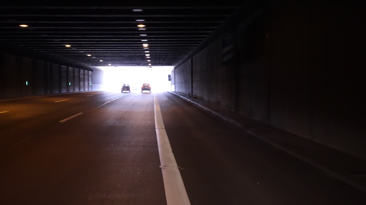 Ripresa di un tunnel in movimento in avanti al rallentatore con pareti scure e un'apertura luminosa che attira l'occhio verso l'uscita.