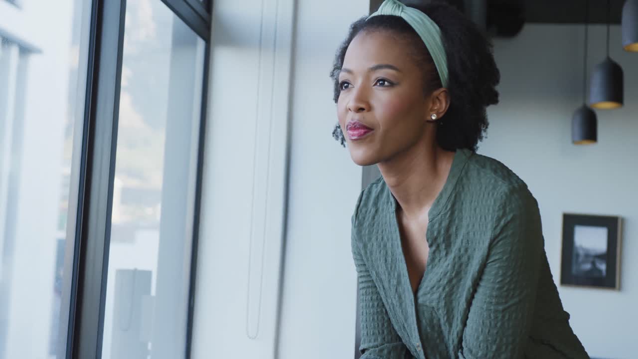 African american businesswoman at window using smartphone alone at office