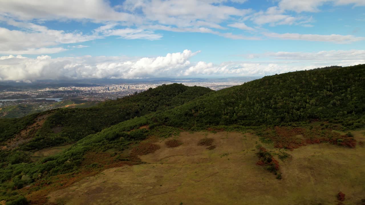 revelando edificios de la ciudad detrás de verdes colinas bajo un espectacular cielo nublado, antena cinematográfica en tirana