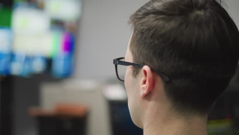 close-up of male video operator sitting at desk in control room, wearing glasses and focusing on multiple monitors. broadcasting, production work in high-tech environment