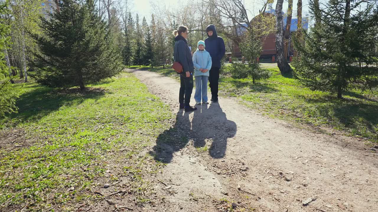 Perhe kävelee ja seisoo polulla aurinkoisessa puistossa