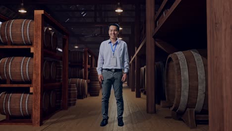 full body of an asian male professional worker standing in cellar of winery, he look at the camera and smiling