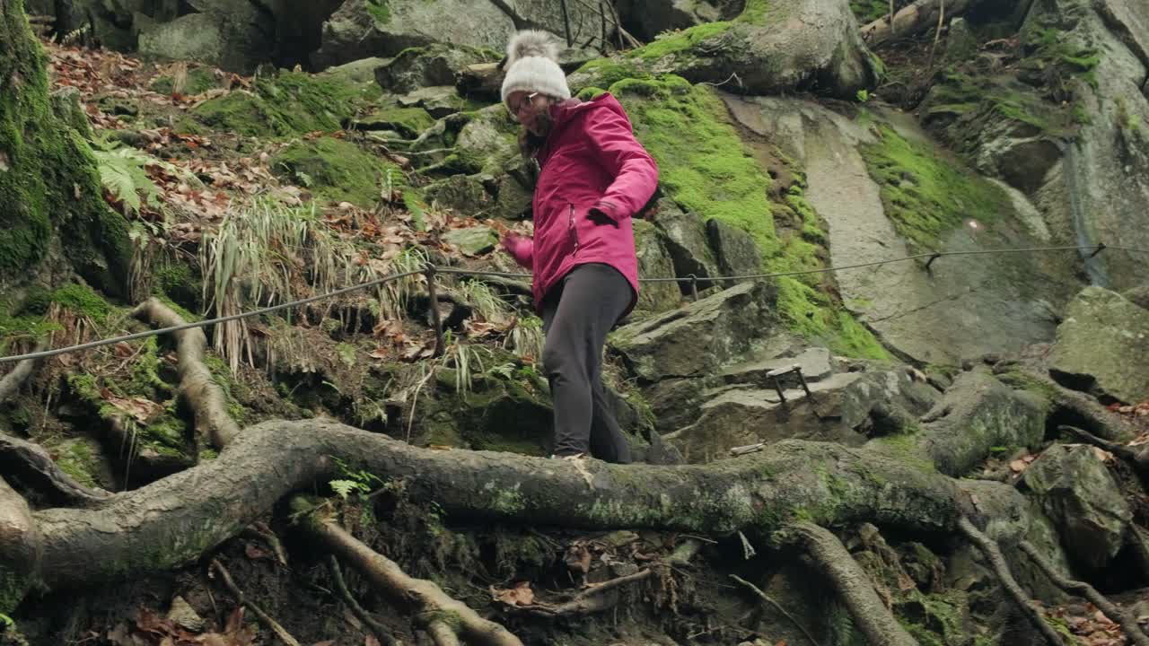 Lady walking down steep section on a hike through the forest. Holding on to a wire helping her walk down branches in the winter. Waterfall of Veliki Sumik in the eastern part of Slovenia