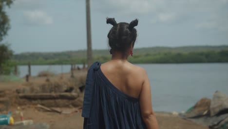 A-woman-in-a-stylish-dress-walking-towards-a-pier-next-to-a-calm-lake