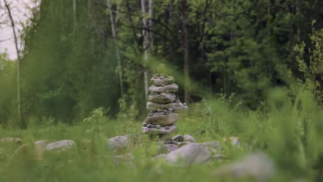 Natural-stacked-rock-pile-statue-in-a-forest-with-scattered-stones-and-grass-in-the-foreground