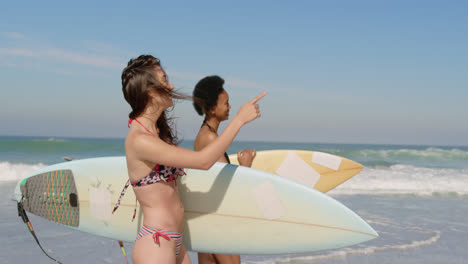 amigas jóvenes caminando con una tabla de surf 4k