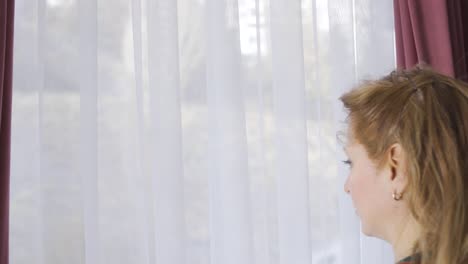una mujer madura pensativa mirando por la ventana desde casa.