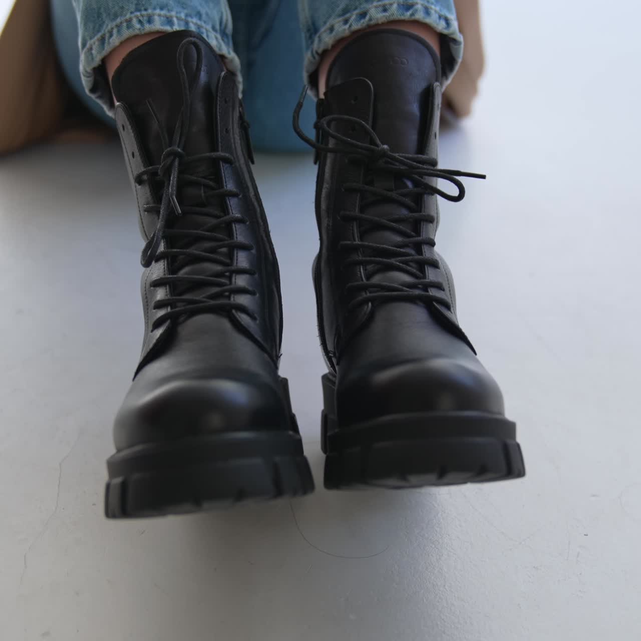 Black combat ankle boots on tractor soles with laces. Close up. Female model in jeans and coat demonstrates warm footwear