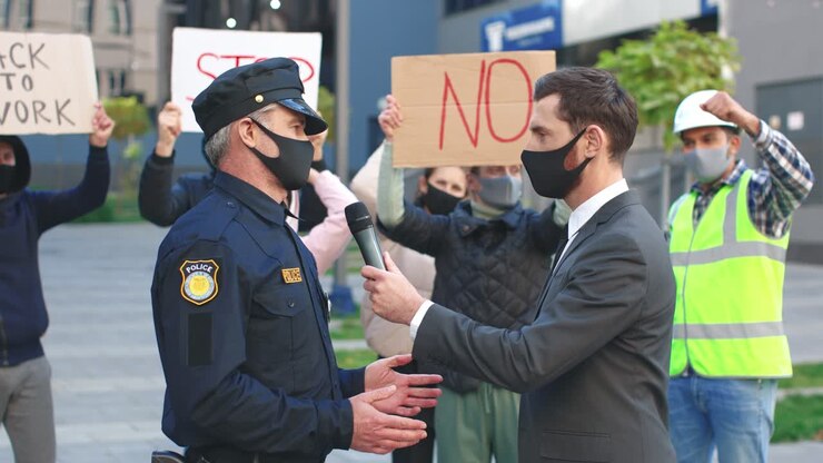 Caucasian journalist or correspondent wearing protective mask in a interview with policeman in a protest against Covid 19