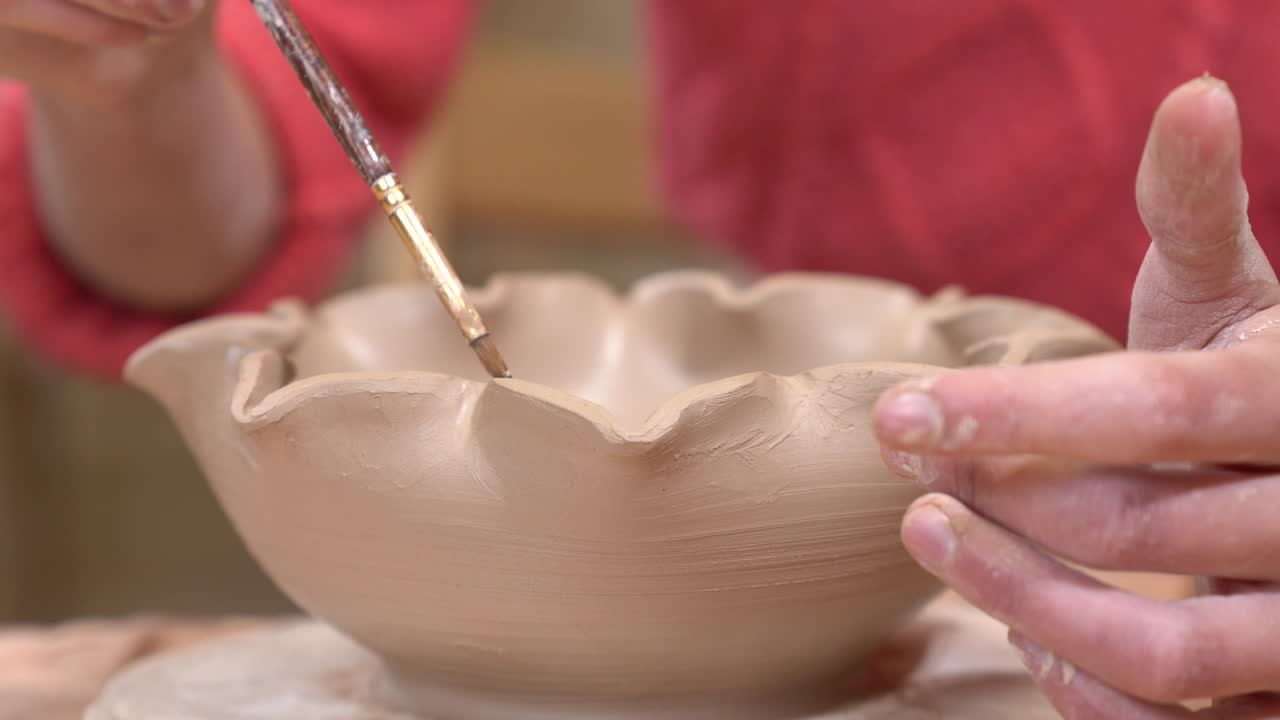 Closeup view of a ceramist smoothing the clay pot edges using the tassel.