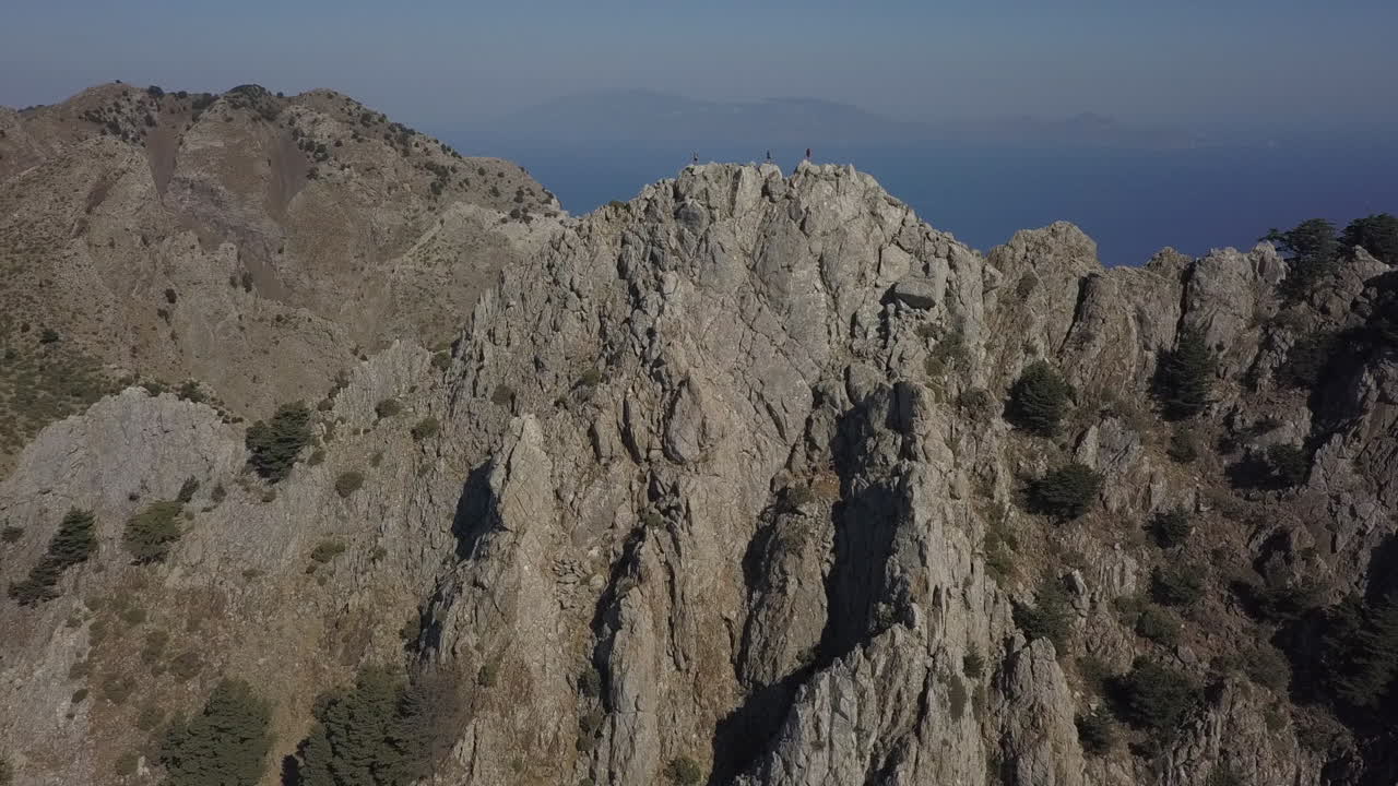 Hikers on rugged summit of Mt Dikeos with blue Mediterranean Sea below