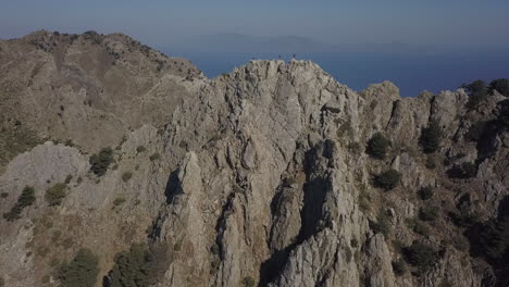 hikers on rugged summit of mt dikeos with blue mediterranean sea below