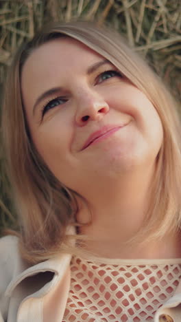 mujer con camiseta y chaqueta se apoya contra la bala de heno con una sonrisa suave y cálida, la luz del sol arroja un brillo suave en su rostro, creando un momento de paz y serenidad en un paisaje rural abierto