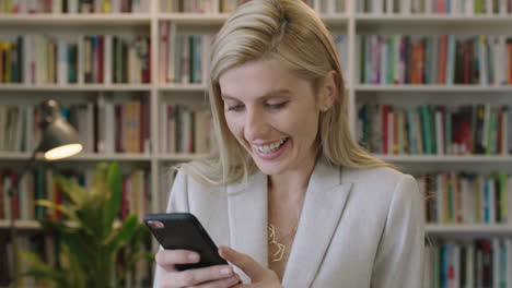 Retrato-De-Cerca-De-Una-Elegante-Mujer-De-Negocios-Rubia-Sonriendo-Disfrutando-De-Mensajes-De-Texto-Navegando-En-Línea-Usando-La-Aplicación-De-Redes-Sociales-Para-Teléfonos-Inteligentes-Usando-Traje-En-La-Oficina-De-La-Biblioteca