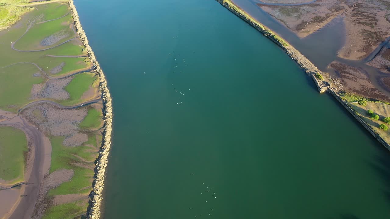 aerial shot over an estuary of blue waters contained by old dams in which you can see coastal birds and on both sides there are green and brown marshes on a sunny summer day in Cantabria Spain