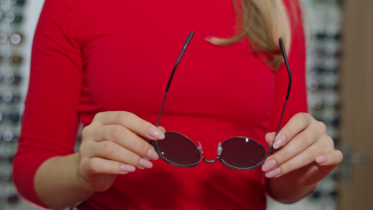 Cute girl with new glasses in shop. Young woman choosing sunglasses in store