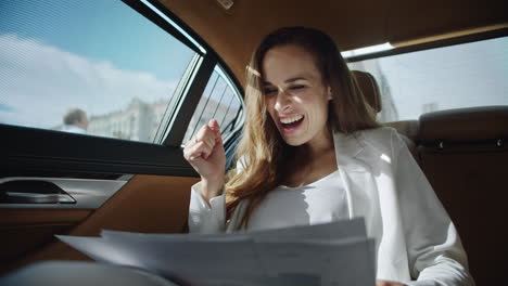 Portrait-of-excited-business-lady-surprising-at-data-in-documents-in-modern-car.