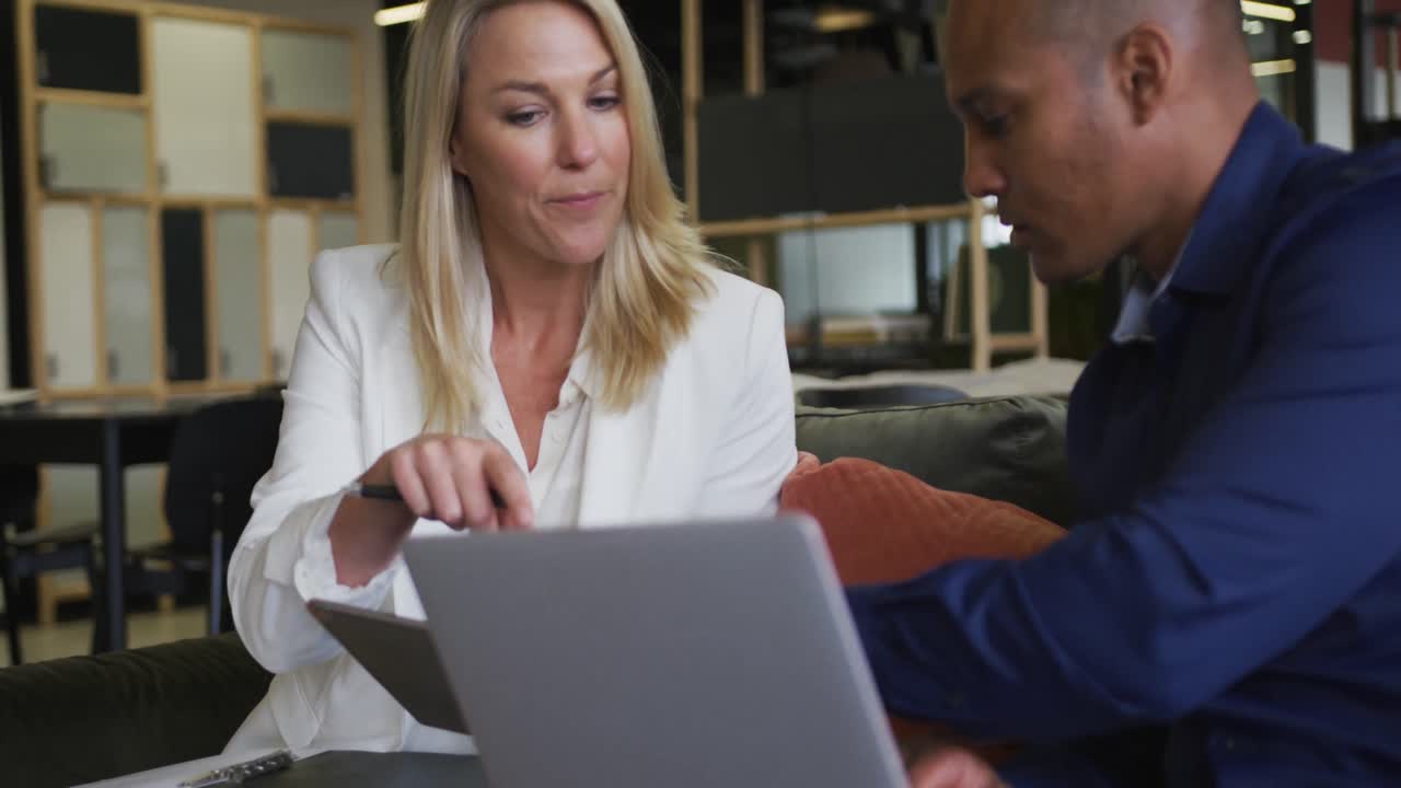 Two diverse business colleagues using laptop and discussing in a casual meeting