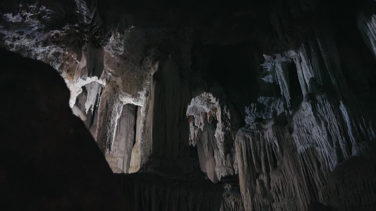 Exploring a dark cave with flashlights reveals stunning stalactites and natural rock formations. Dramatic underground scenery highlights geological textures and mysterious beauty