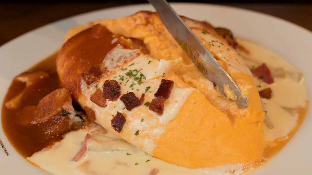 Knife slices open fluffy Japanese omelette rice, revealing creamy interior, under warm restaurant lighting