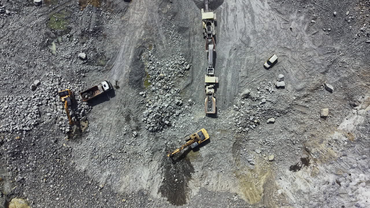 Workers operate heavy machinery to extract granite at a busy quarry during daytime
