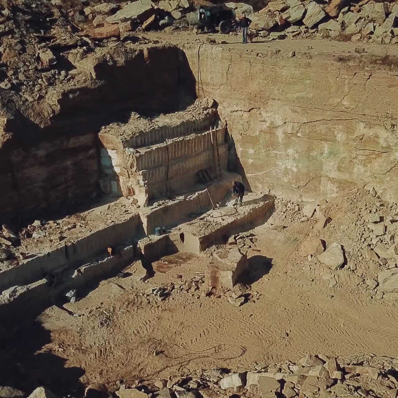 worker is drills stones with using pneumatic tool in the sand quarry. Camera motion up. Aerial view