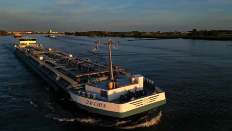 Filmische-Drohnenaufnahme,-Die-Um-Das-Schiff-Bacchus-Kreist,-Das-Durch-Die-Stadt-Zwijndrecht-Segelt,-Und-Sonnenlicht,-Das-Darauf-Fällt,-Und-Die-Gebäude-Am-Fluss-Mit-Seeverkehr-Im-Hintergrund