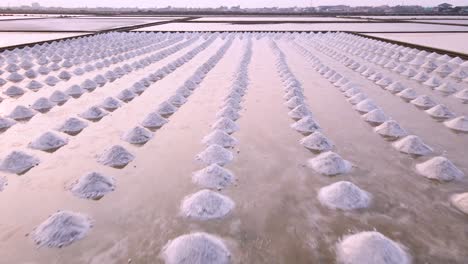 tilt down aerial shot over sea salt piles in thailand with pink sunset skies