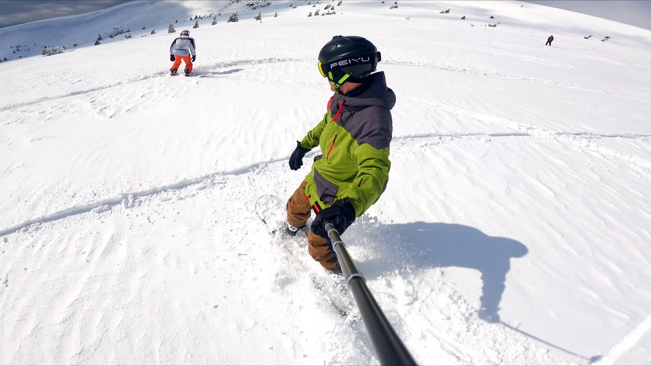 Selfie footage of a ride on the snowboard. Sportsman records himself riding down and his fellow at backdrop.