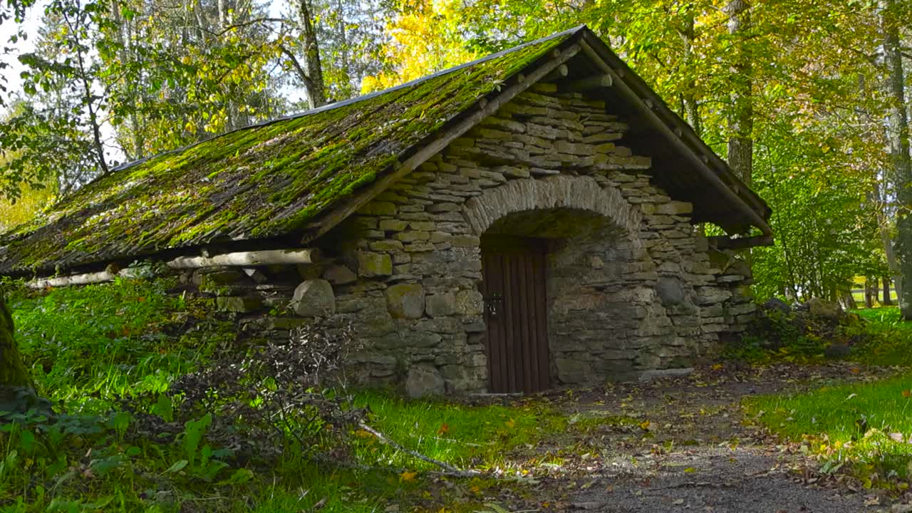 Small stone structure house built from limestones in Saku mansion park during late summer or autumn while leaves are golden yellow and some are on the ground. Sun is shining on the mossy eternite roof