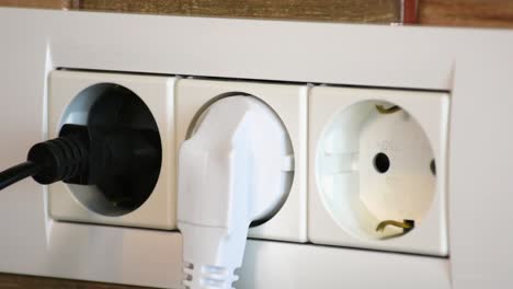 man inserts power cables into electrical wall socket