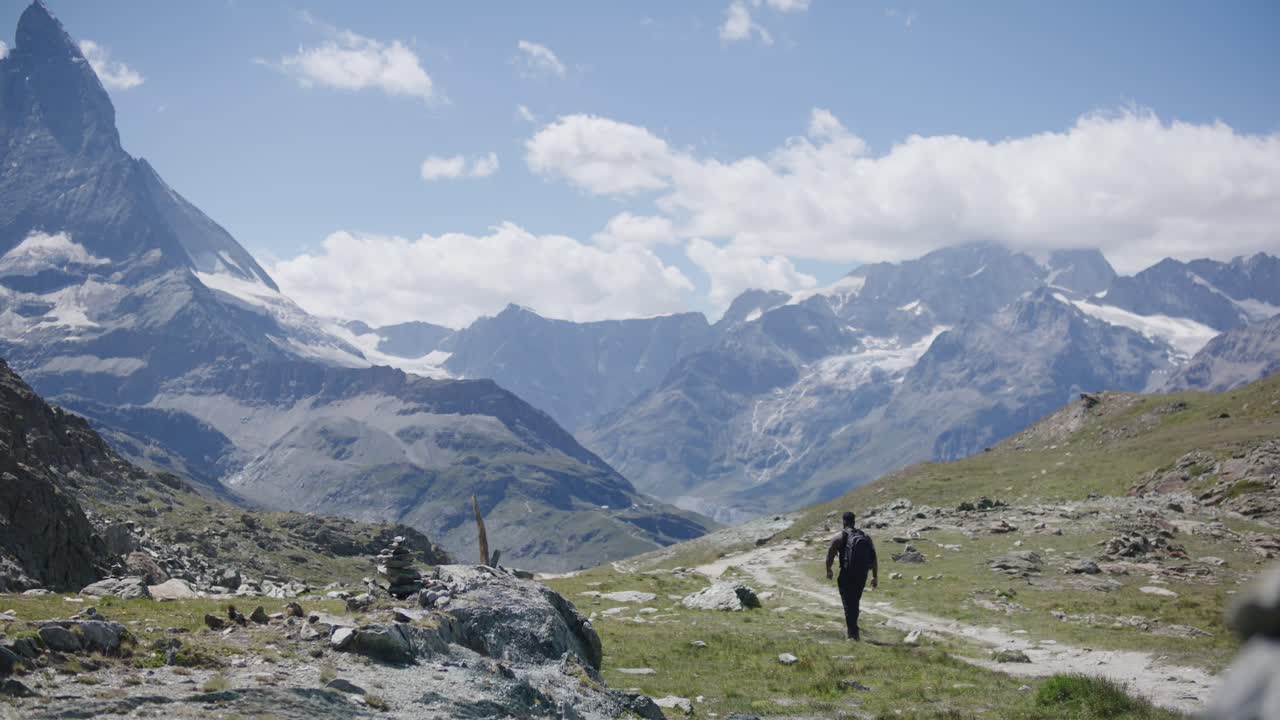 Viajante negro com mochila olhando ao redor do penhasco explorando a paisagem montanhosa perto do Matterhorn na Suíça