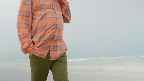 Low-angle-view-of-active-senior-African-American-man-talking-on-phone-while-walking-at-beach-4k