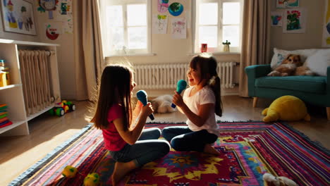 two young girls sing and dance playfully with toy microphones at home