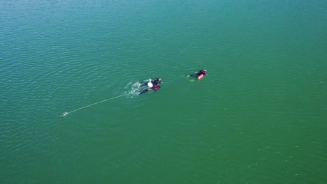 aerial rotating shot of scuba divers swimming back to shore in the lac du crès