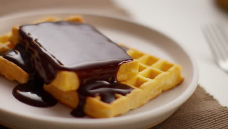 close up of person eating stack of waffles covered in melted chocolate sauce on plate