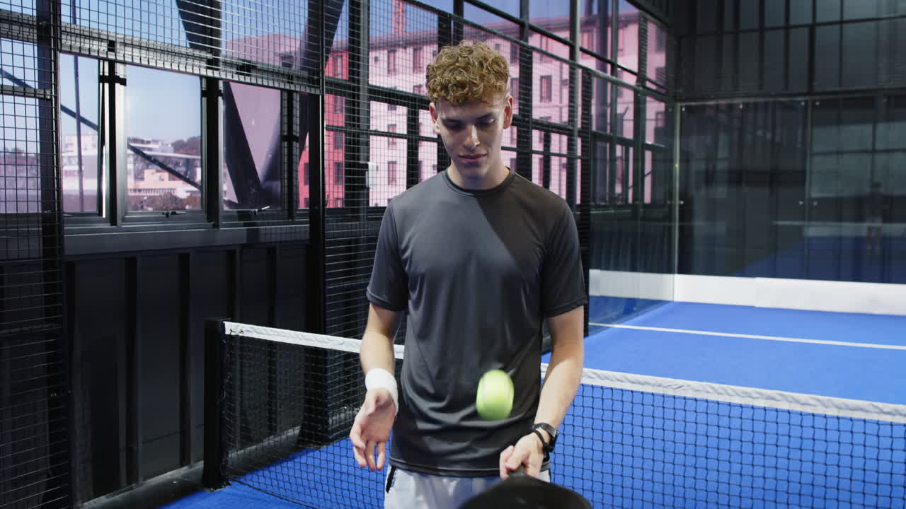 Young man holding padel racket on indoor court, preparing for match, copy space