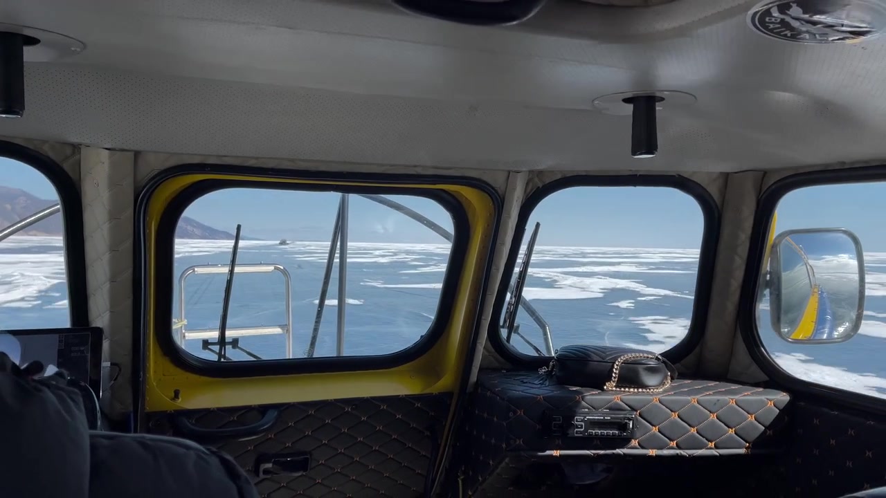 Innenansicht aus einer Luftkissenbootkabine, die sich über rissiges Eis und Schnee auf dem Baikalsee in Sibirien, Russland, bewegt, mit weitem Winterhorizont, der durch die Fenster sichtbar ist