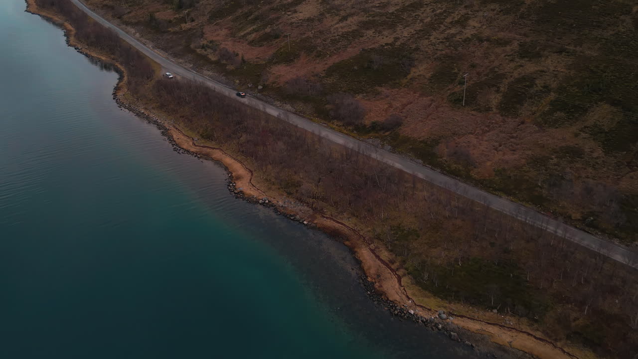 Bil kører hurtigt på vej langs søbredden ved solnedgang om efteråret