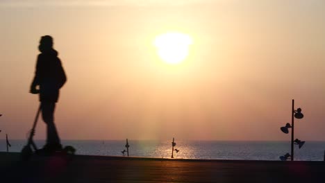 man on electric scooter briefly stops to admire pink ocean sunrise, exits left