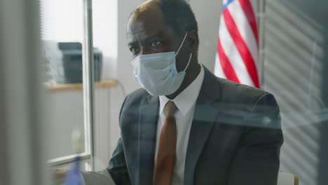 man in a suit wearing a mask, reviewing documents in an office.