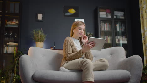 mujer joven feliz viendo una película divertida en una tableta y riendo mientras se sienta en un sofá en casa